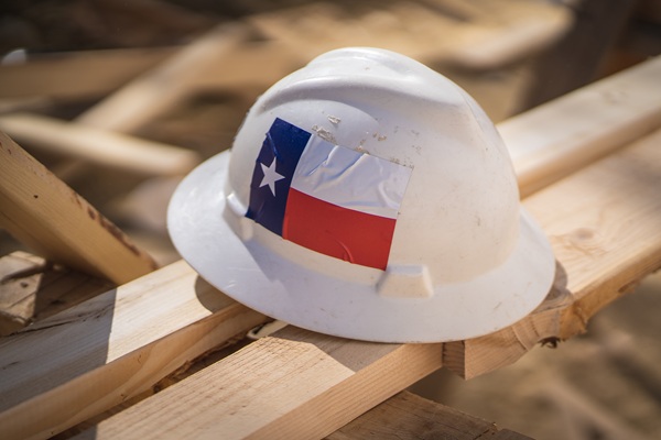 Construction hat with Texas flag sticker on planks of wood at construction site.