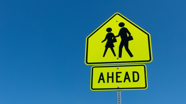 Yellow pedestrian crossing sign with the word “Ahead” against a clear blue sky.
