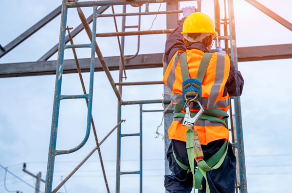 Construction worker wearing a safety harness and helmet while climbing scaffolding at a job site.