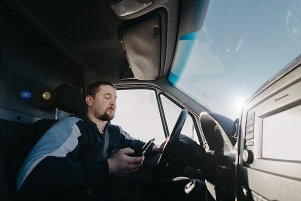A man driving a commercial truck, looking down and texting on his smartphone instead of watching the road.