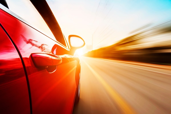 Low-angle side view of a red car speeding down a Texas highway at sunset with a motion blur effect.