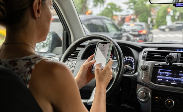 A driver using both hands to type on a smartphone while sitting in traffic, a violation of statewide texting while driving laws that carry significant penalties in Texas.